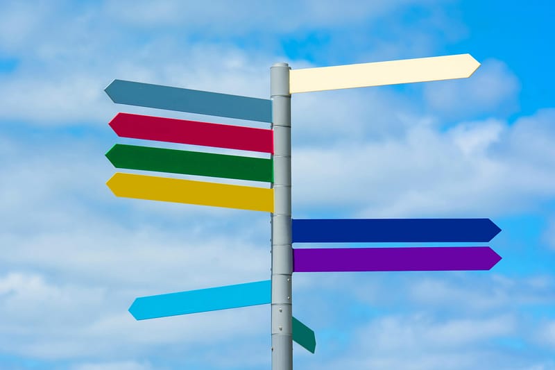 A signpost with colorful directional arrows pointing in different directions against a blue sky