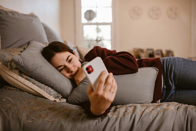 A woman resting on a bed while looking at her phone